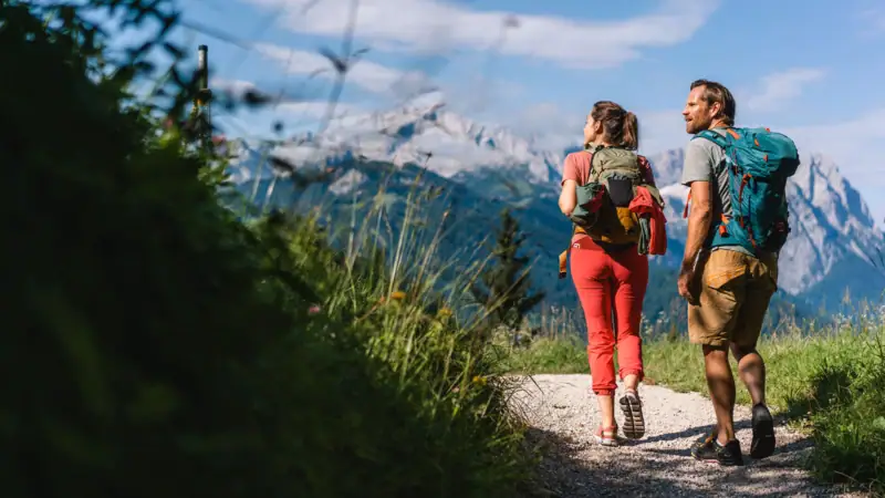 A man and a woman walk along a path with mountains in the background.