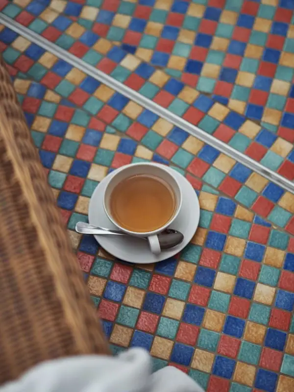 A cup of tea on a saucer placed on a colorful tile floor.