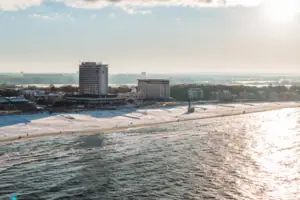 aja Warnemünde Strand mit dem aja Warnemünde und Schnee im Vordergrund, bewölkter Himmel im Hintergrund.