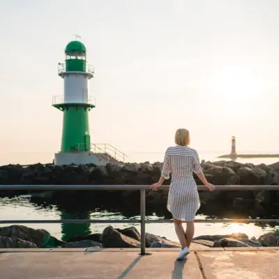 A woman is standing on a jetty next to a green and white lighthouse.