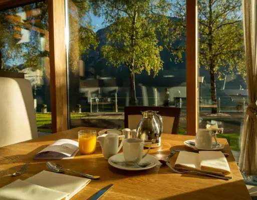 Breakfast A table with a teapot and cups in front of a glass wall.