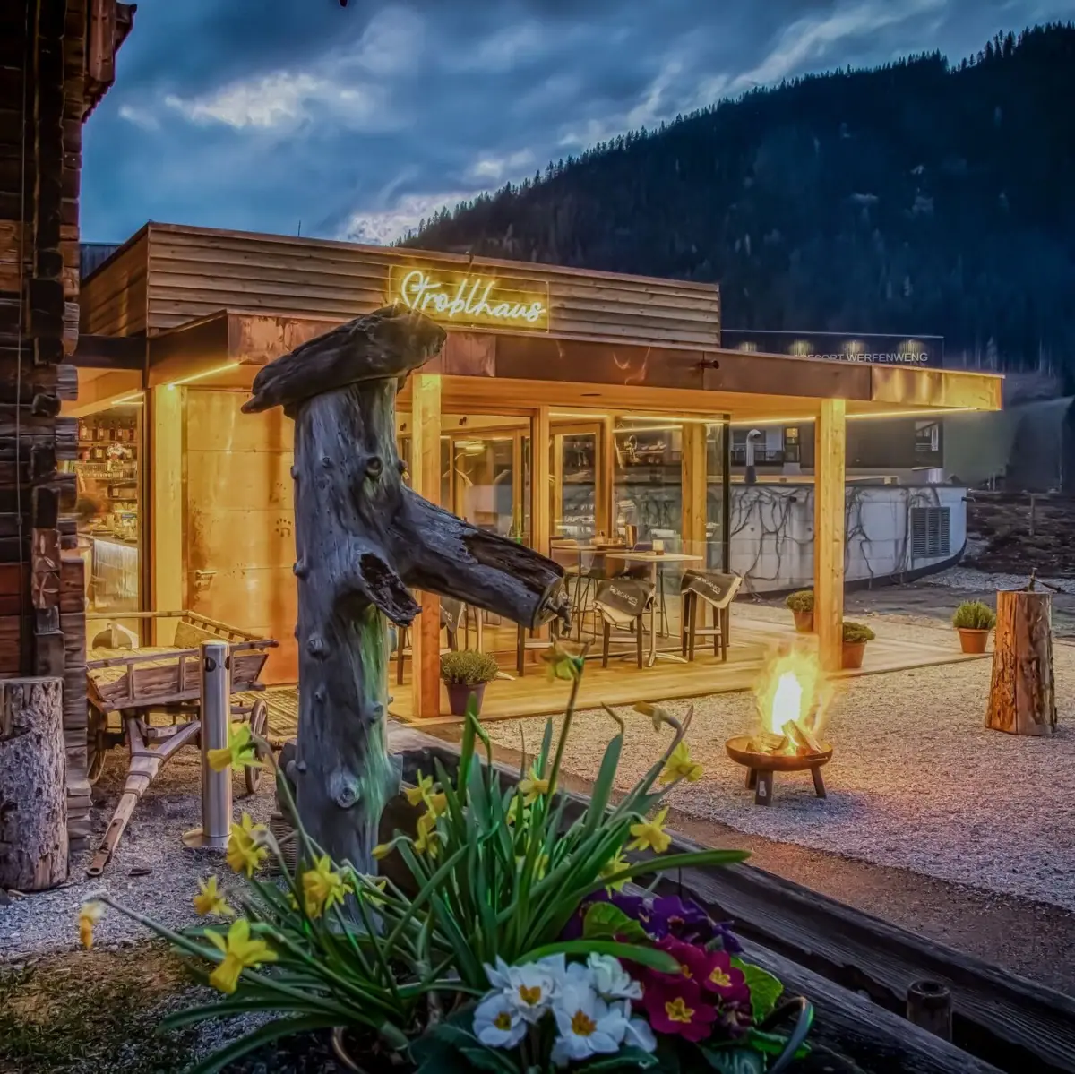 A building with a fire pit and a tree stump in front of it.