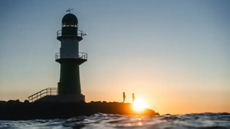 A lighthouse in the water at sunset.