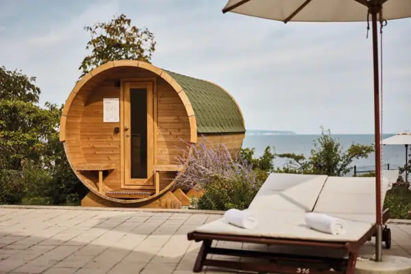 A barrel sauna next to a deckchair and a pool.