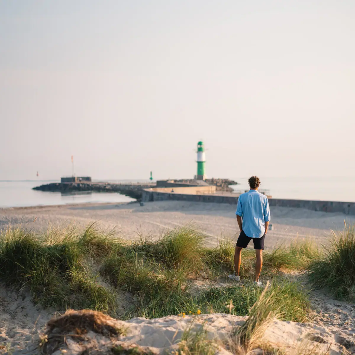 A man stands on the beach and looks at a lighthouse.