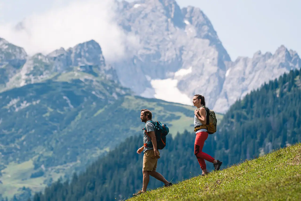 Hiking Garmisch Two people hiking on a hill with mountains in the background.
