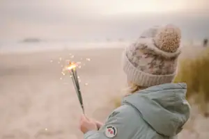 A girl holds sparklers on the beach.