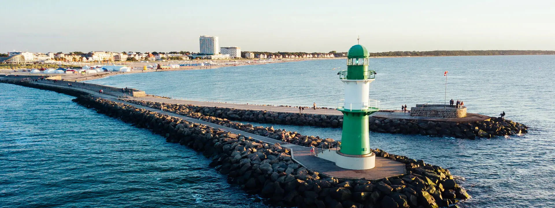 Green and white lighthouse on rocky waterway.