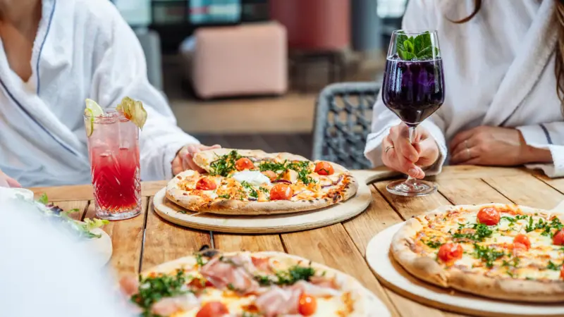 A group of people sitting at a table enjoying pizzas and drinks.