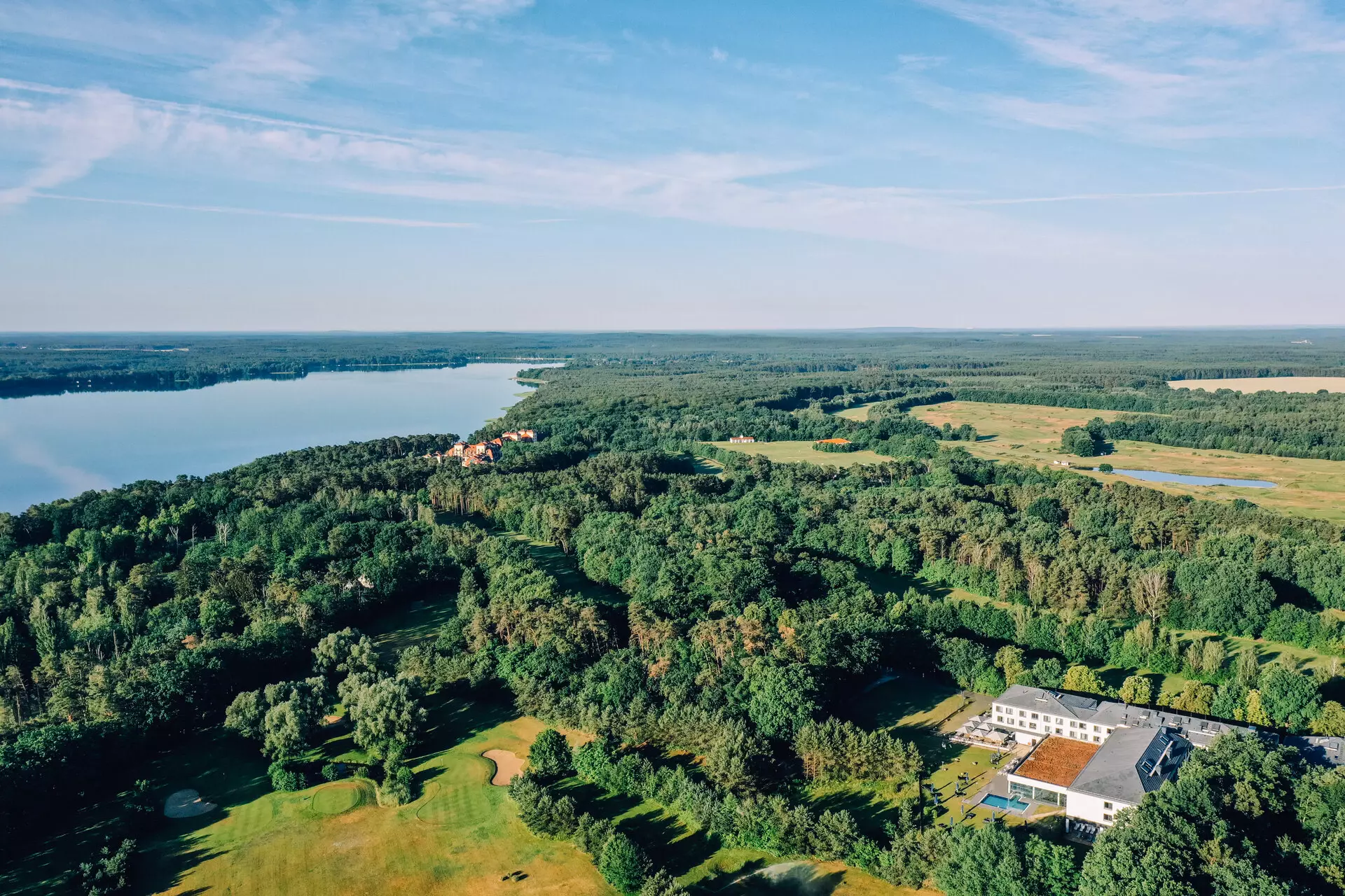 aja Bad Saarow Aerial view of a large expanse of water with surrounding trees and a building.