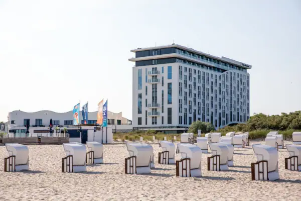 Beach chairs are lined up in front of a white building on the beach and the sun is shining. 