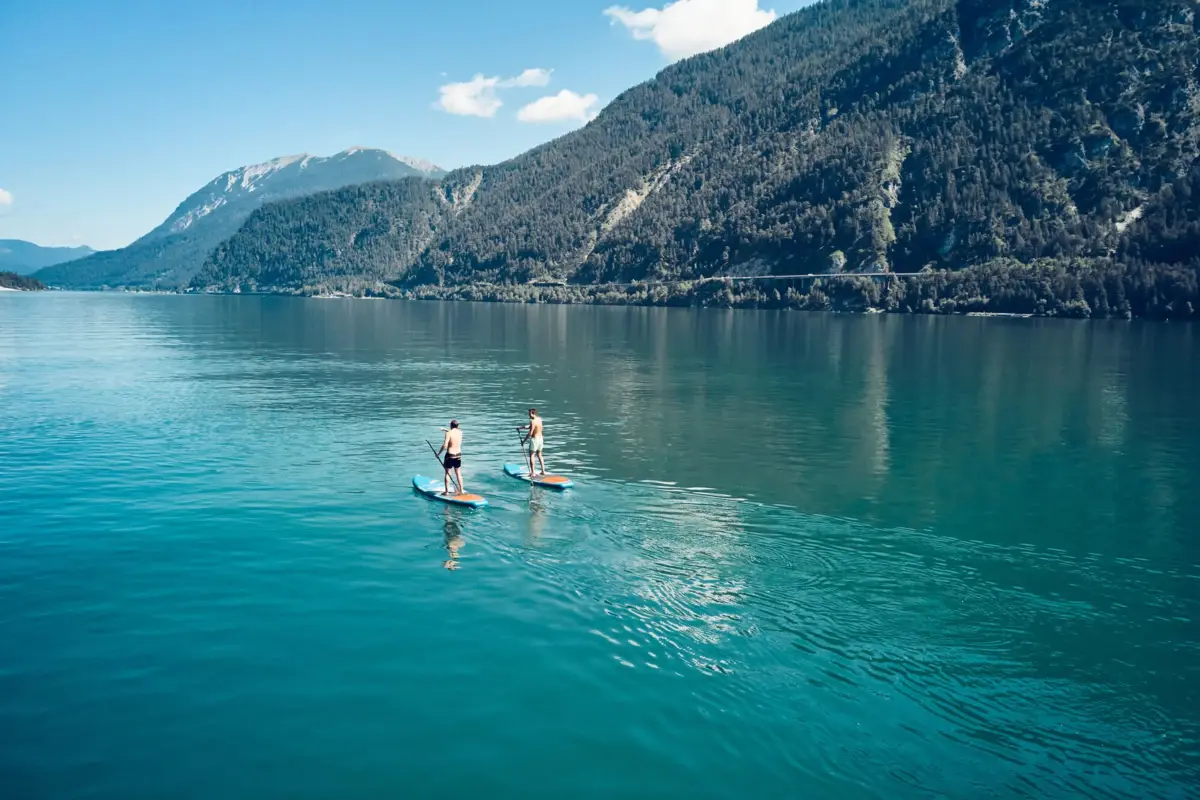 Two people on paddleboards on a lake with mountains in the background.