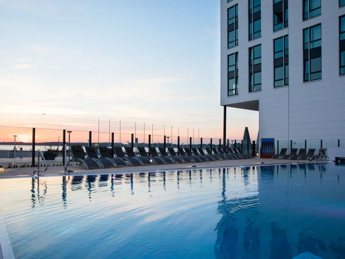 Outdoor pool aja Travemünde A pool with chairs and a building in the background.