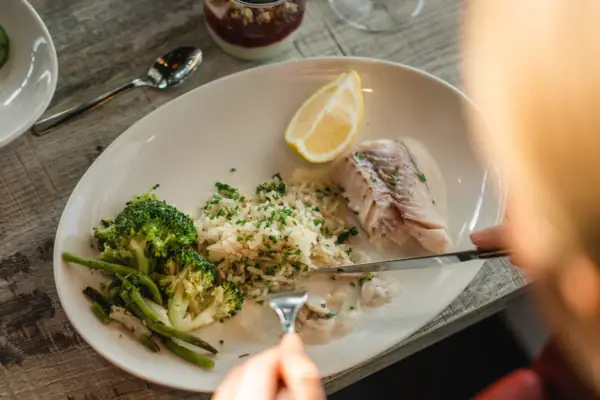 One person eats from a plate filled with broccoli, fish, lemon and rice.
