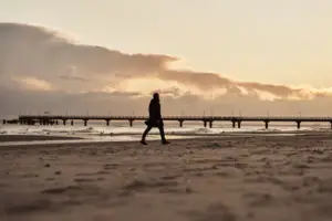 A person walks along the beach at sunset.