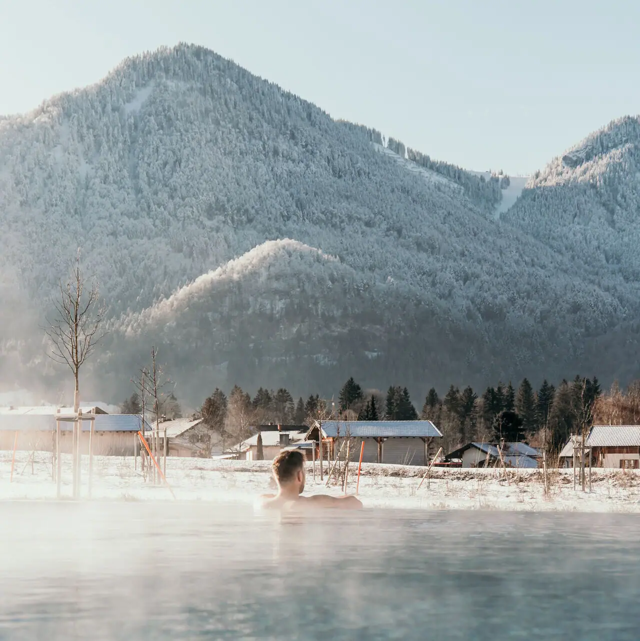 Outdoor pool in winter A person in a pool with mountains in the background.