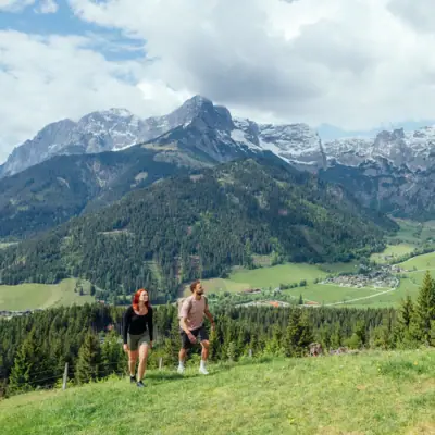 A man and a woman are walking on a hill with mountains in the background.