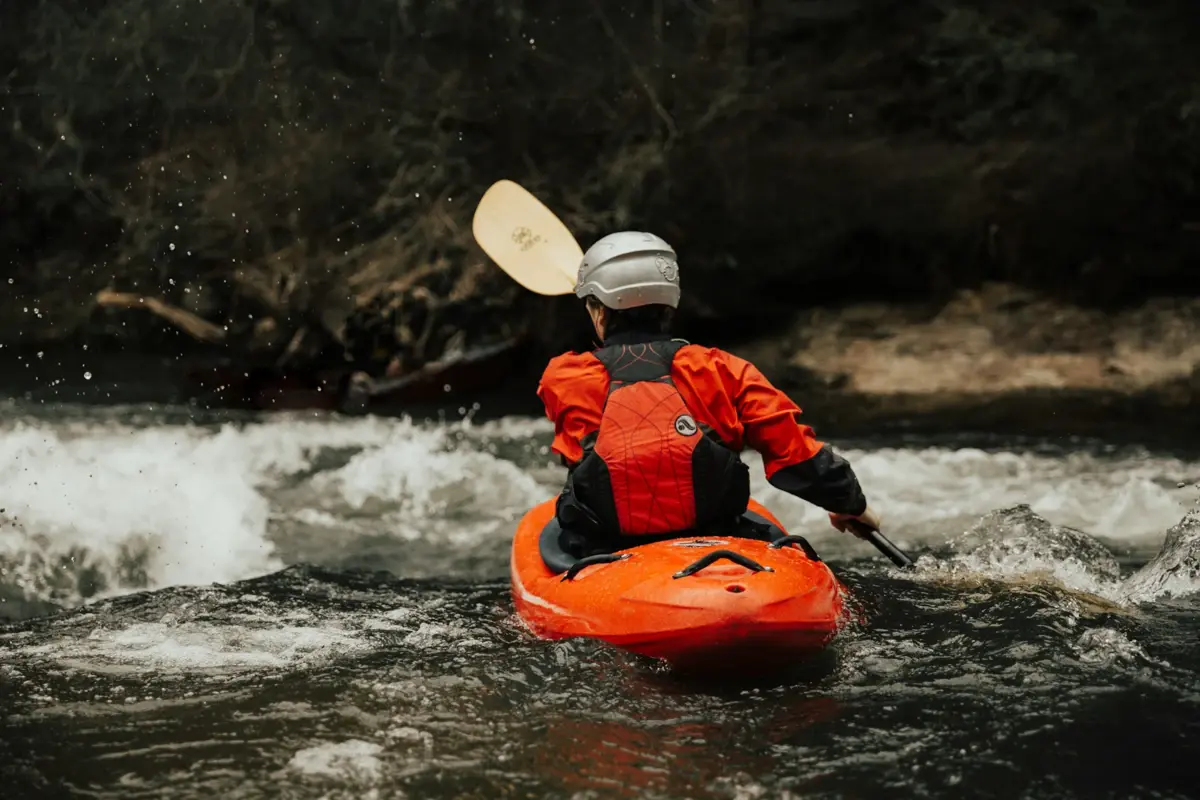 A person in a kayak with life jacket and paddle on a river.