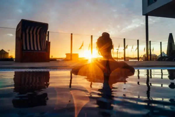 A woman sits in a pool with a sunset in the background.