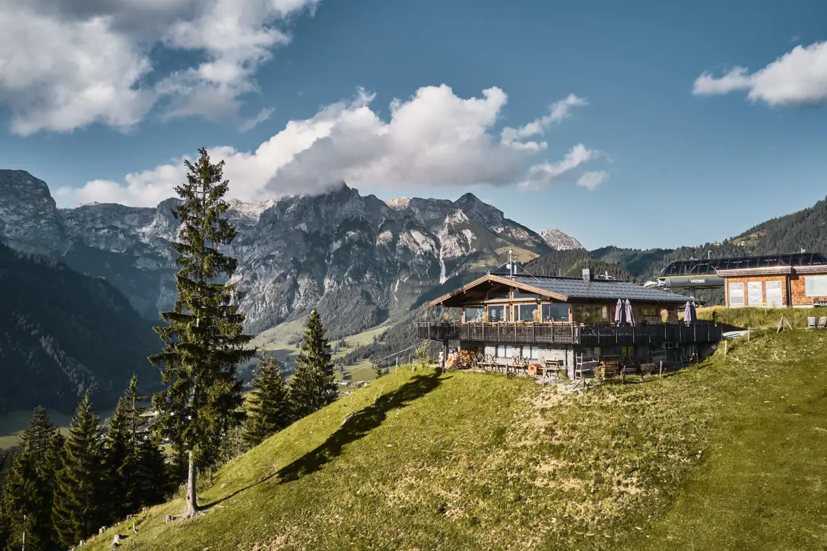 Werfenweng A hut on a hill with mountains in the background.