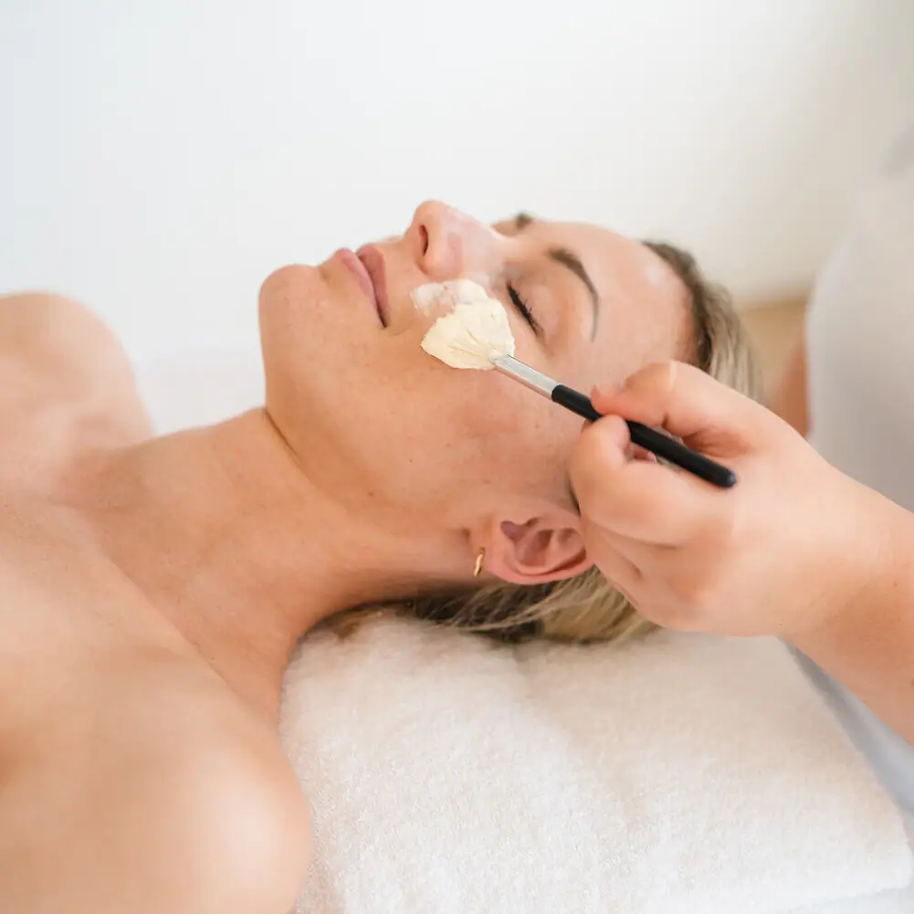 A woman lies with a paintbrush on her face.