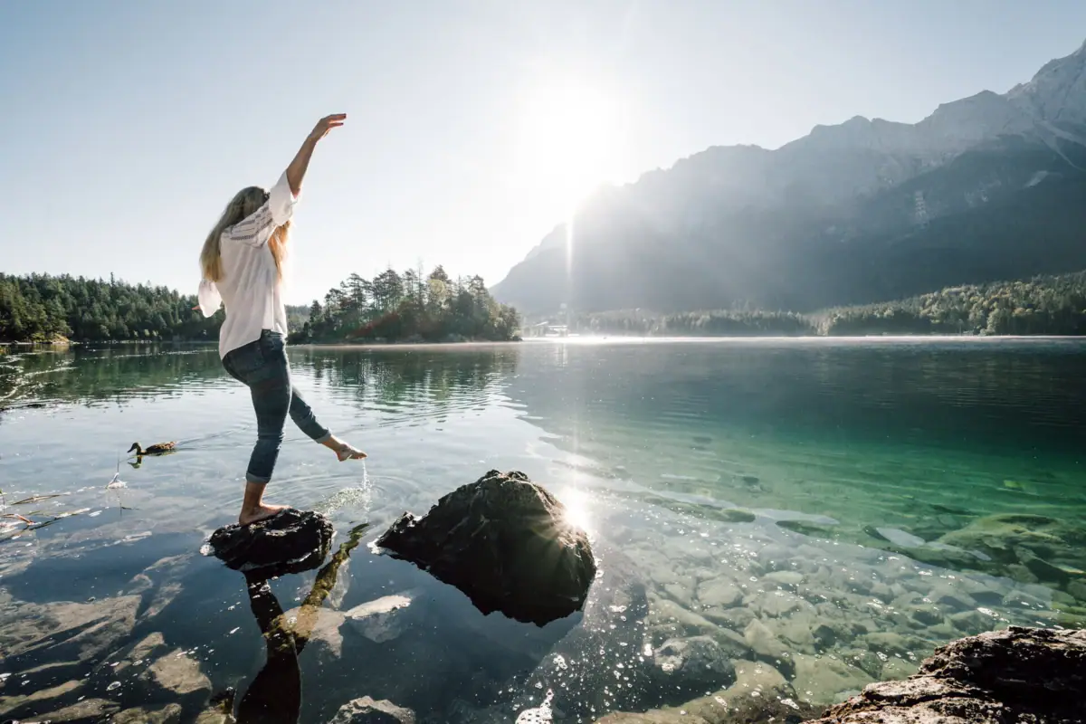 A woman stands on a rock in a body of water and raises her arm.