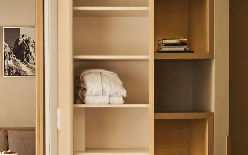 There are two white bathrobes on a shelf.