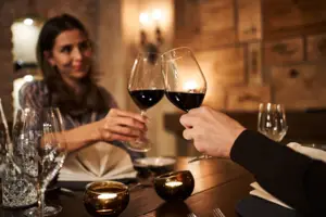 A man and a woman clink glasses of wine at a table during a meal.