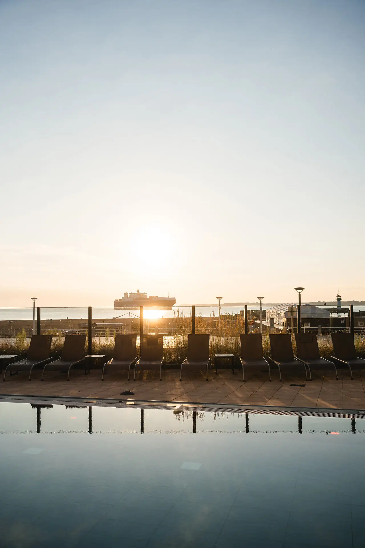 Row of chairs beside a pool under an open sky.