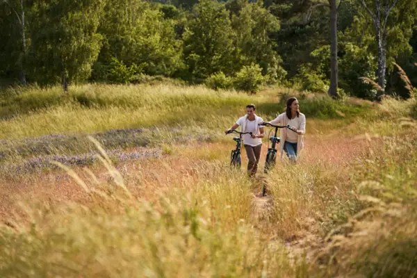 A man and a woman are walking through a field on bicycles.