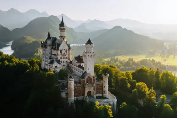 Neuschwanstein Castle A castle on a hill with trees and mountains in the background.