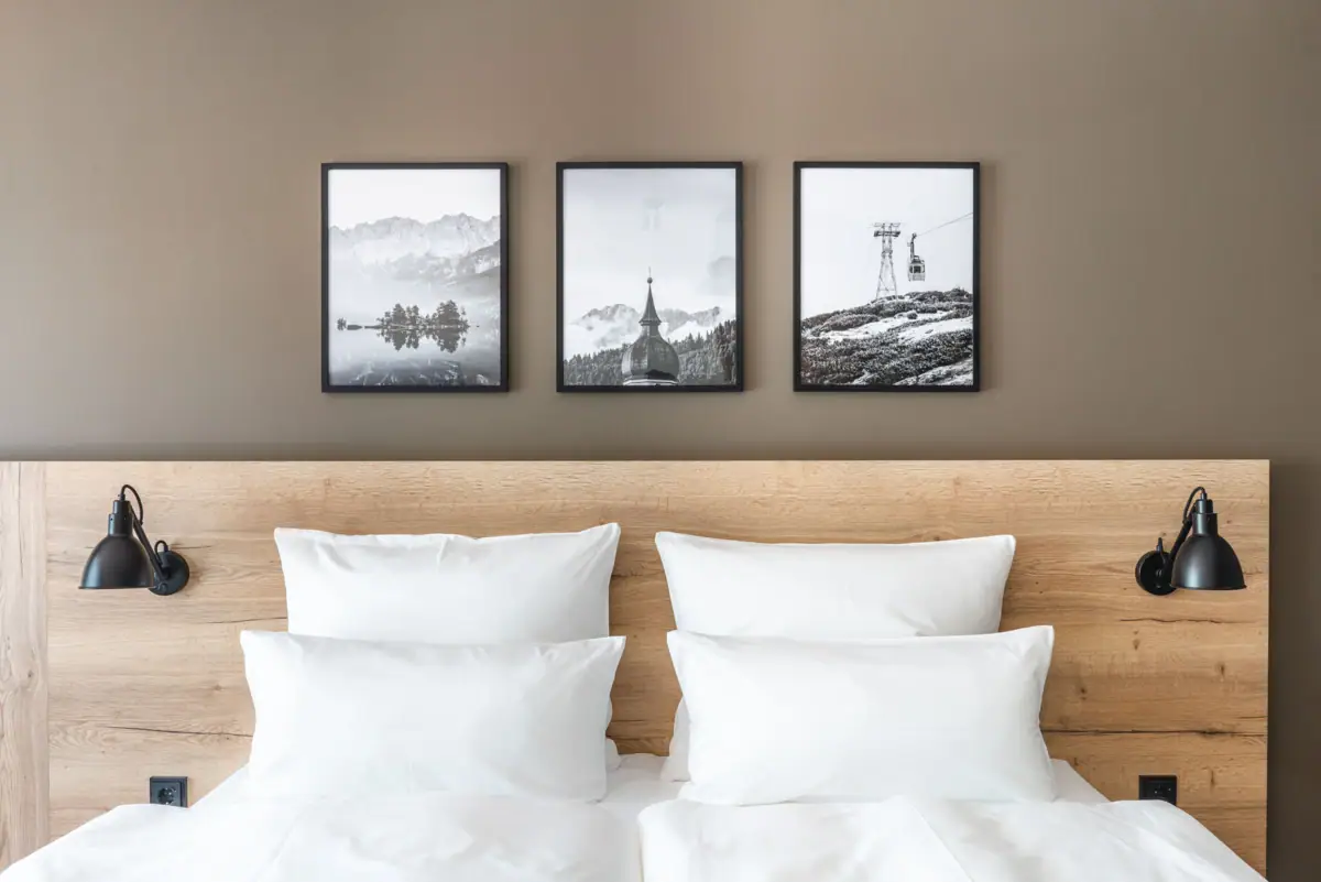 Room Bed with white cushions and wooden frame, in the background a picture of a mountain and a ski lift.