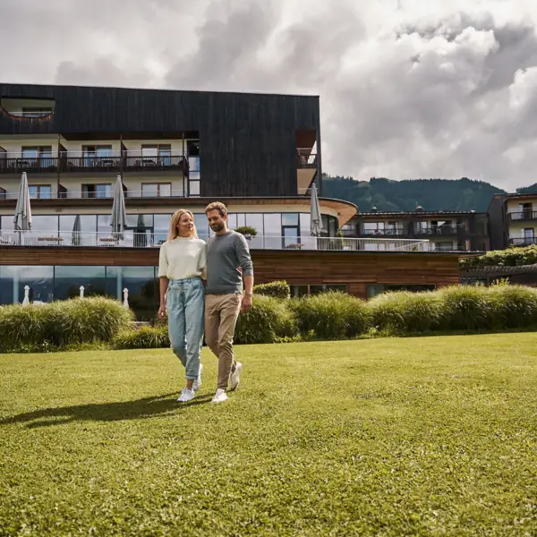 A man and a woman walk across a lawn with the hotel in the background.
