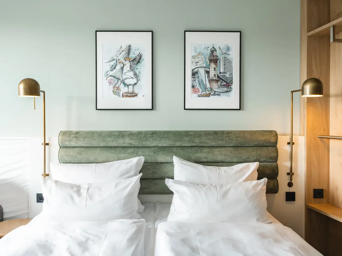 A bed with white cushions and a green headboard, flanked by two lamps.