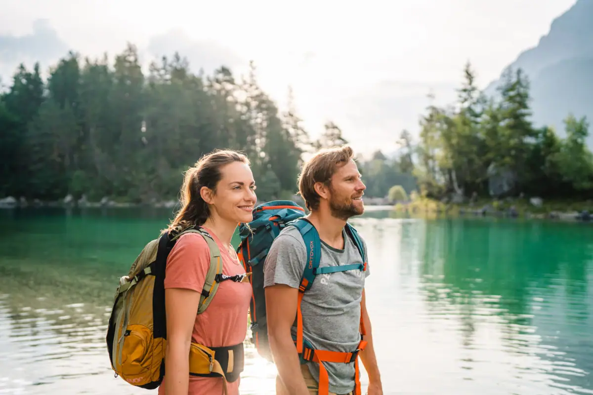 Eibsee hike A man and a woman with rucksacks are standing in front of a body of water.