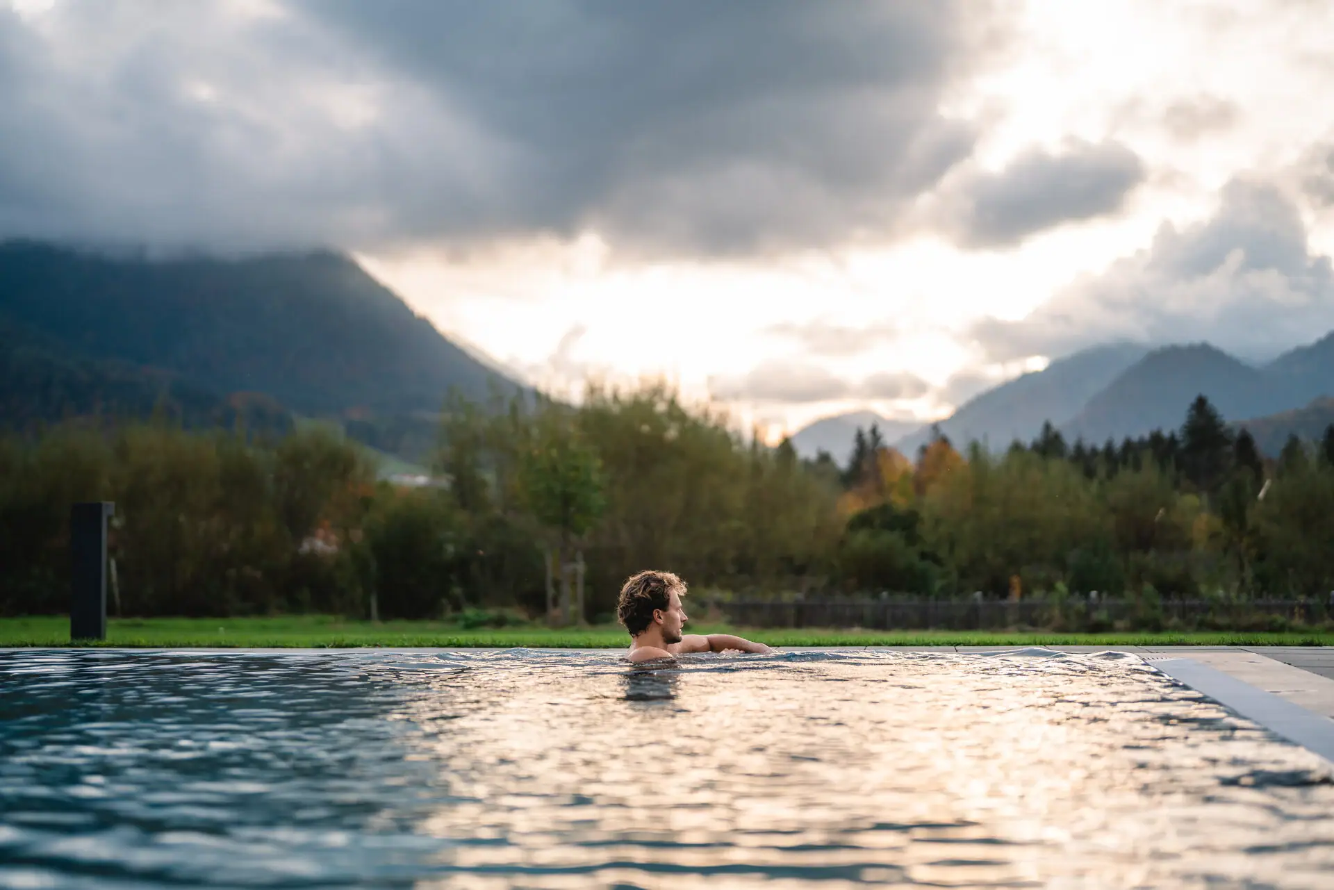 A man swimming in a pool with mountains in the background under a partly cloudy sky.