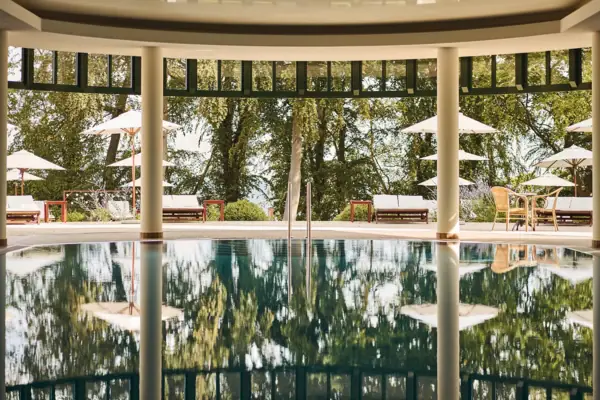 A swimming pool with parasols and chairs in the background.