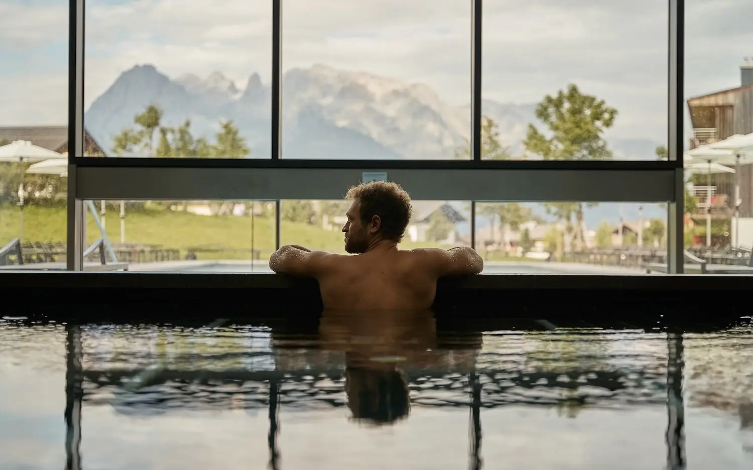 Man swimming in a pool with mountain and tree views.