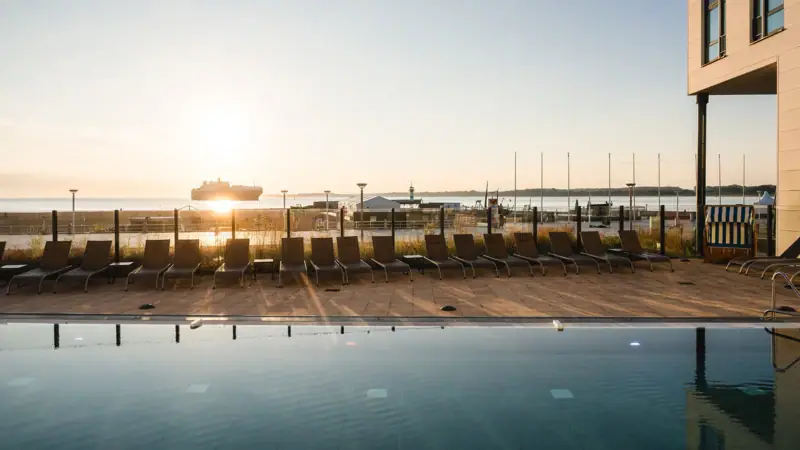 A pool with chairs and a boat in the background.