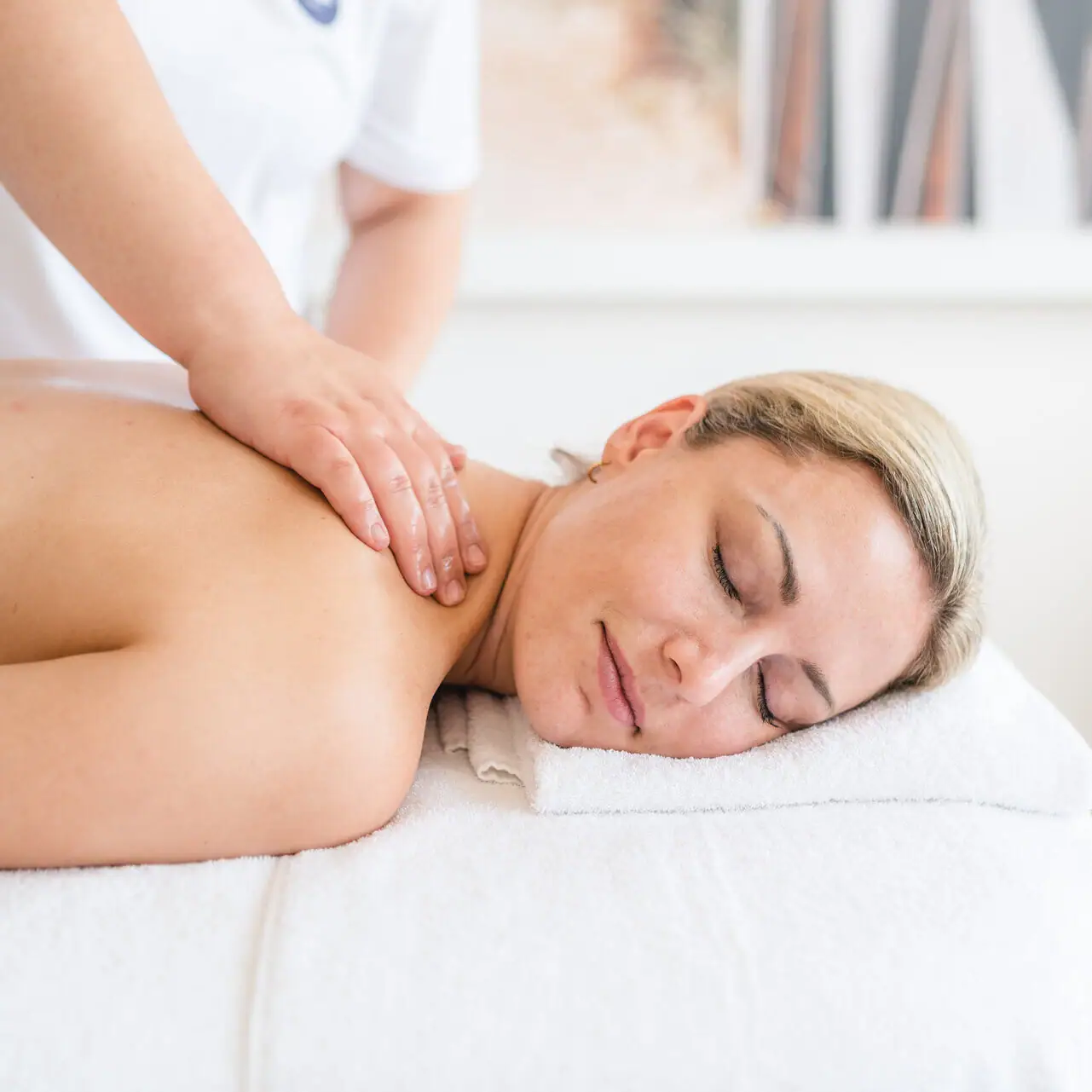 A woman lies on a white towel with her eyes closed.