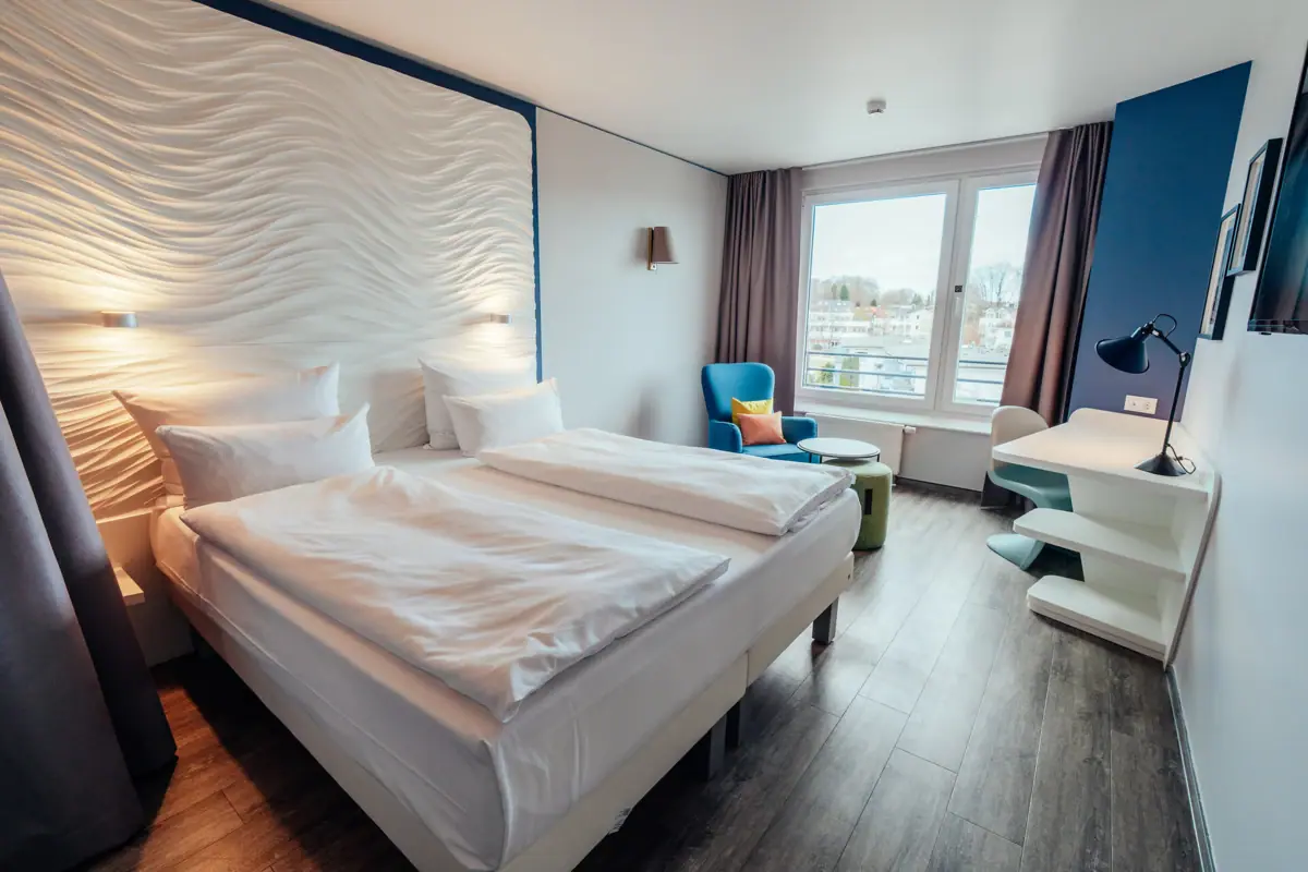 A room with two beds and a table, featuring pillows, bedding, and interior design elements.