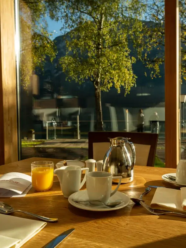 A table with a teapot and cups in front of a glass wall.
