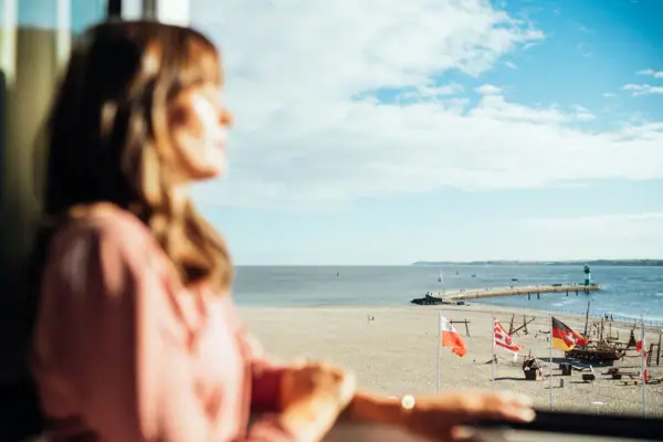 Room view A woman looks out of a window onto a beach.