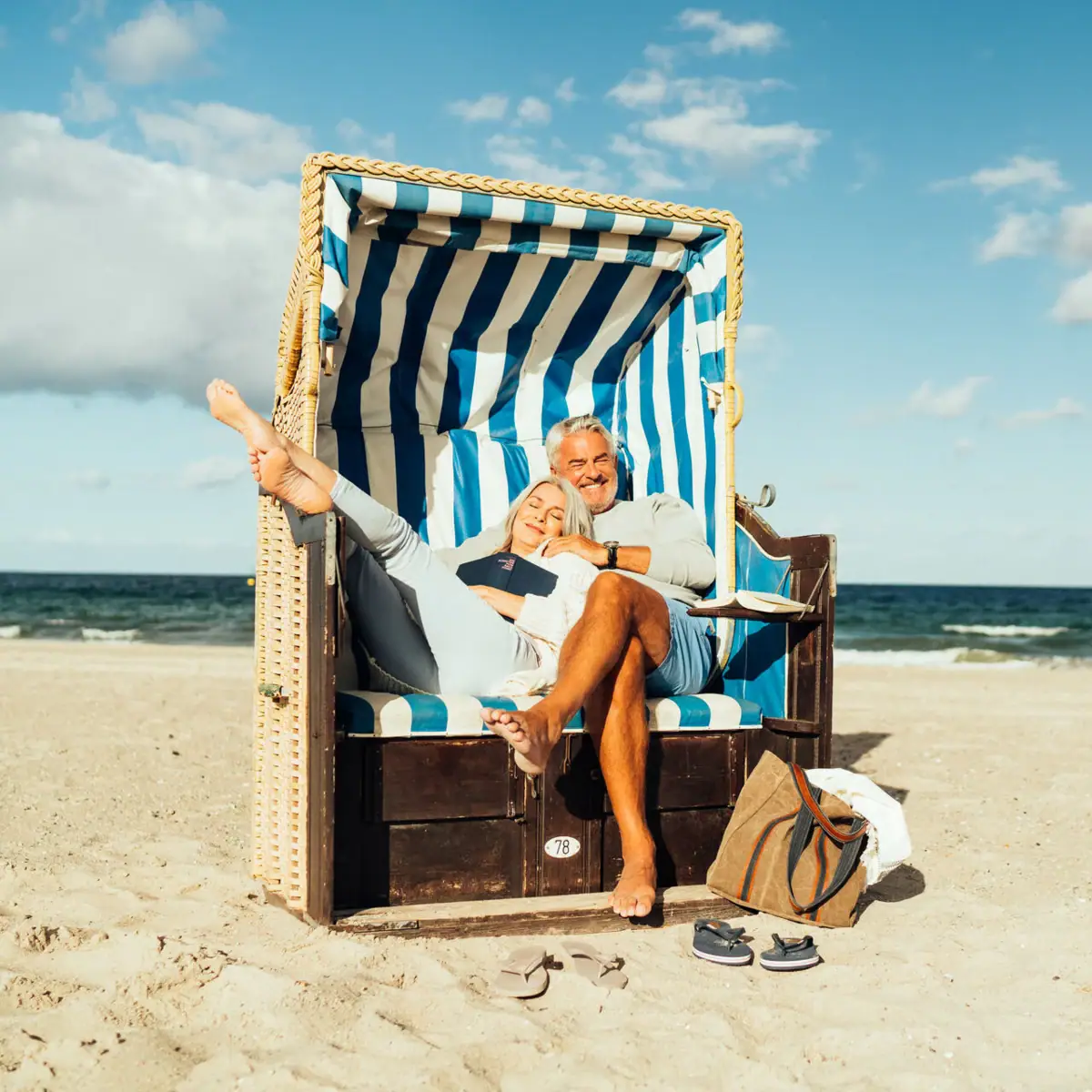 A man and a woman are sitting in a beach chair on the beach.