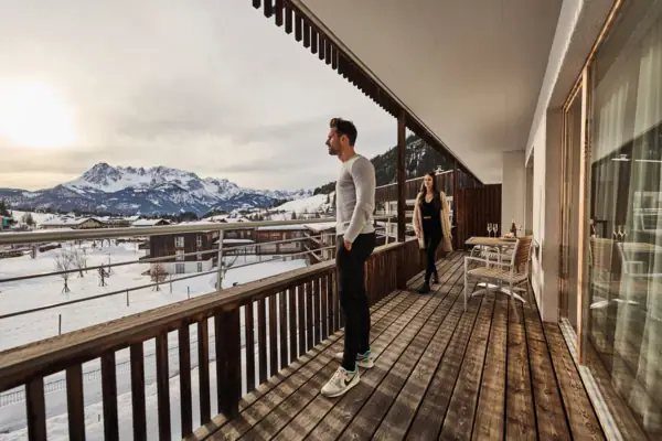 A man and a woman stand on a terrace and look out over snow-covered mountains.