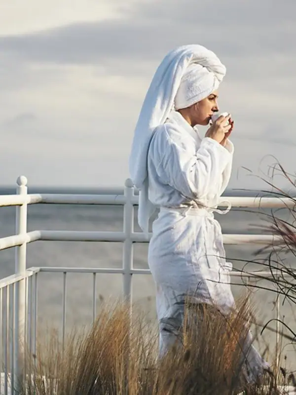 A woman in a bathrobe drinking from a mug.