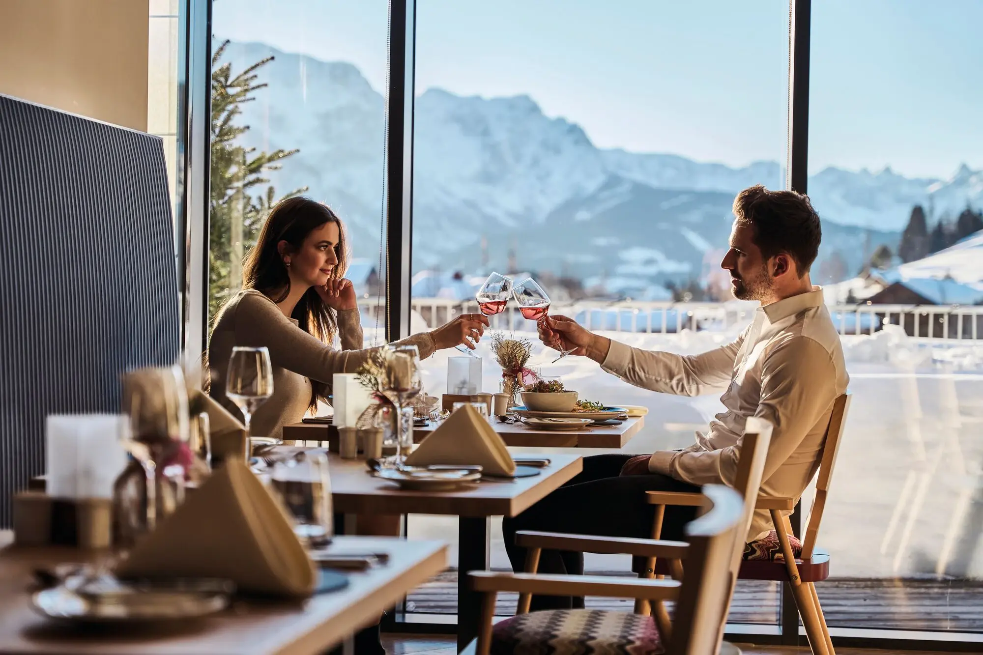 A man and a woman are sitting at an outdoor table holding glasses of wine.