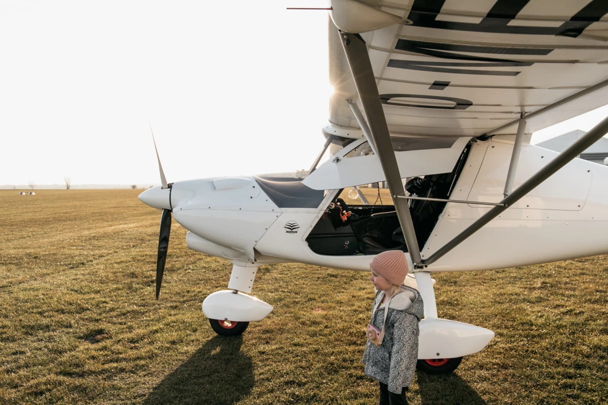 A child is standing in front of a small aeroplane.