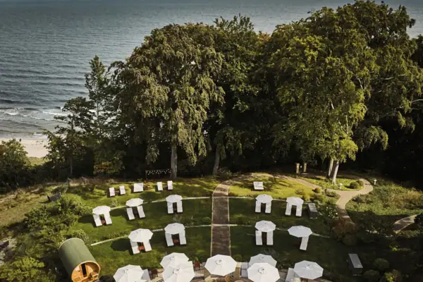 Garden Nordperd & Villas A group of white parasols on a grassy area with trees and the sea in the background.