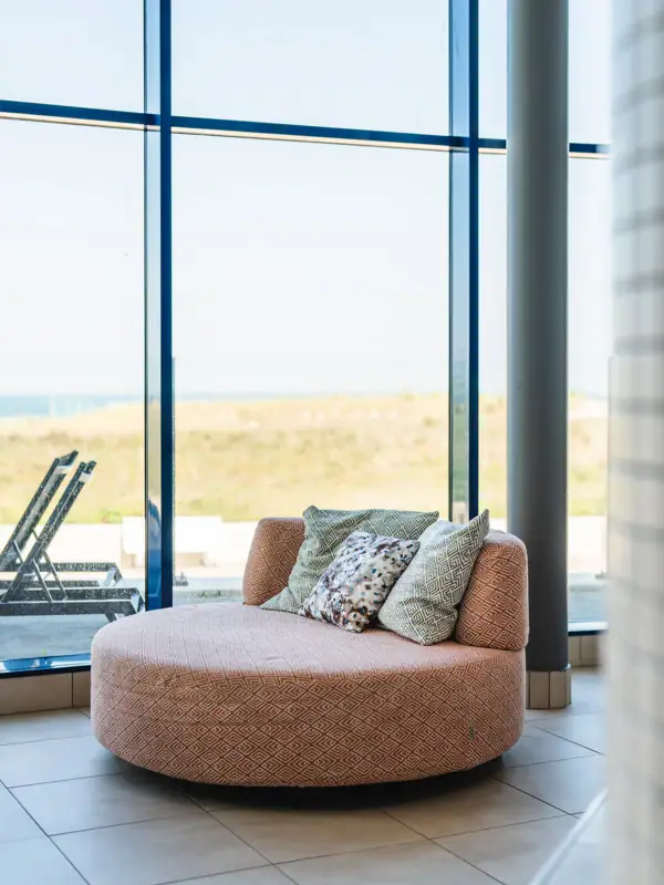 Lounger at aja Warnemünde Round couch with cushions in front of a window.